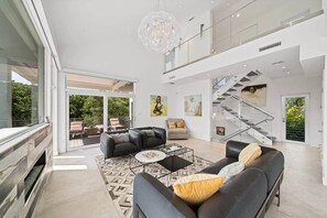 A spacious living area with a modern staircase, a fireplace, and a balcony with outdoor furniture. - Luxurious Retreat At The Whispering Palms (Wabasso Beach)