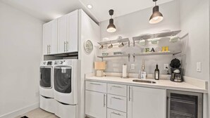 A modern kitchen with built-in appliances, a countertop with a coffee maker, and a wall-mounted shelf with mugs. - Luxurious Retreat At The Whispering Palms (Wabasso Beach)