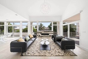 A spacious living room with a large window, a fireplace, and a modern chandelier. - Luxurious Retreat At The Whispering Palms (Wabasso Beach)