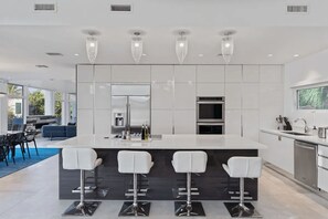 Cocina moderna con una isla central, taburetes de bar, electrodomésticos de acero inoxidable e iluminación colgante.
