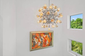 A chandelier, two framed artworks, and a window with a view of greenery. - Luxurious Retreat At The Whispering Palms (Wabasso Beach)