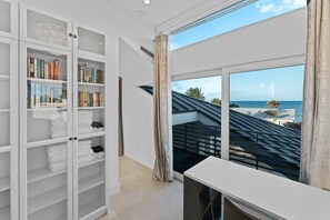 Ein modernes Zimmer mit großem Fenster, einer integrierten Bücherwand und Blick aufs Meer.