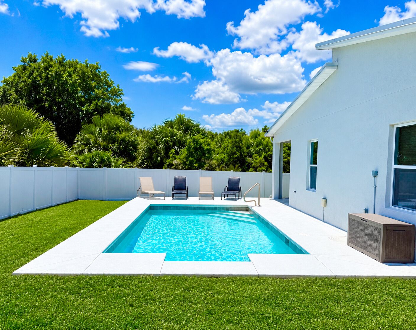 Una piscina con cubierta blanca, rodeada por una cerca blanca y abundante vegetación.
