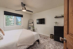 Ein Schlafzimmer mit Bett, Deckenventilator, Fernseher, Kommode und Fenster.