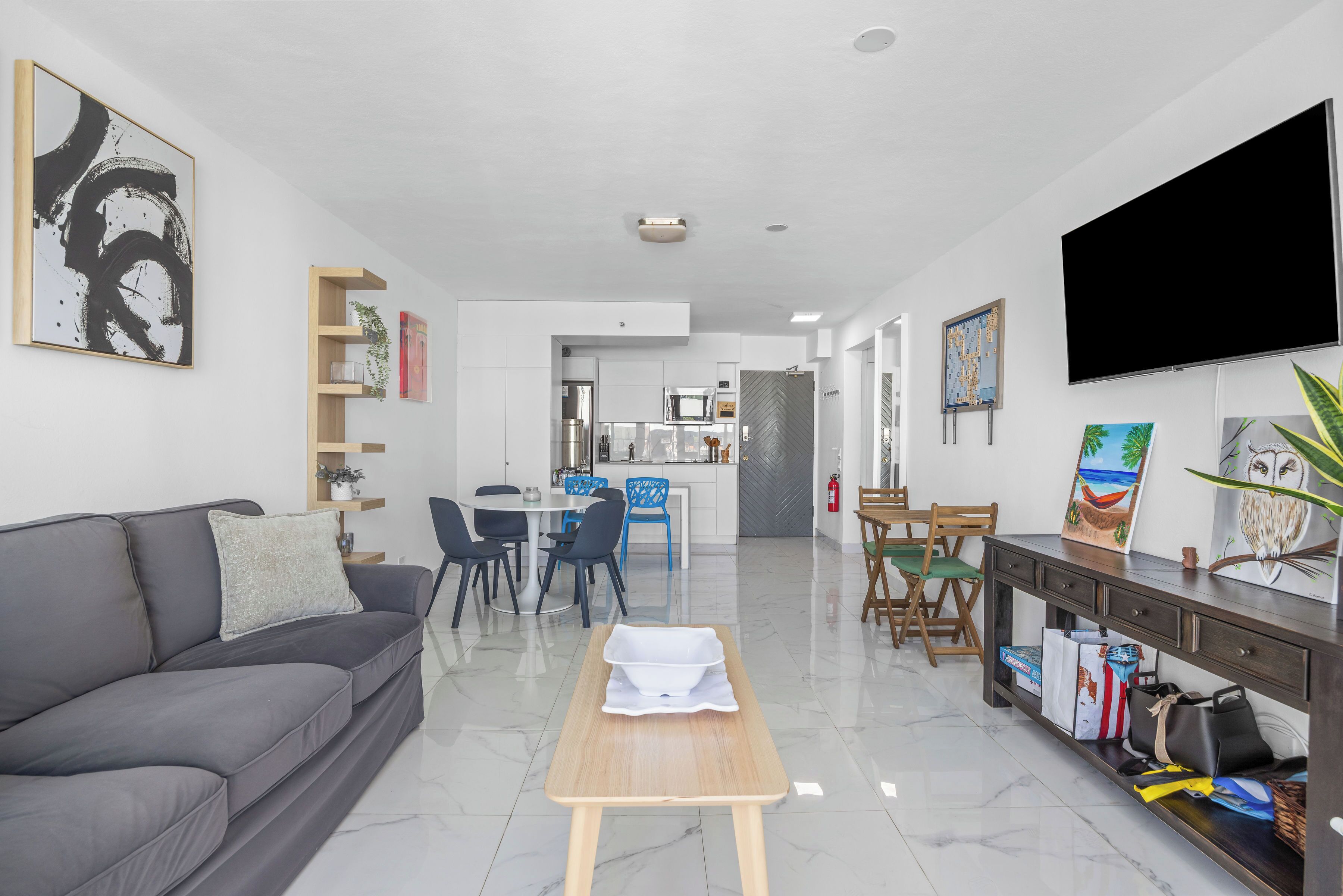 A modern living room with a grey sofa, a wooden coffee table, and a dining area with chairs and a table.