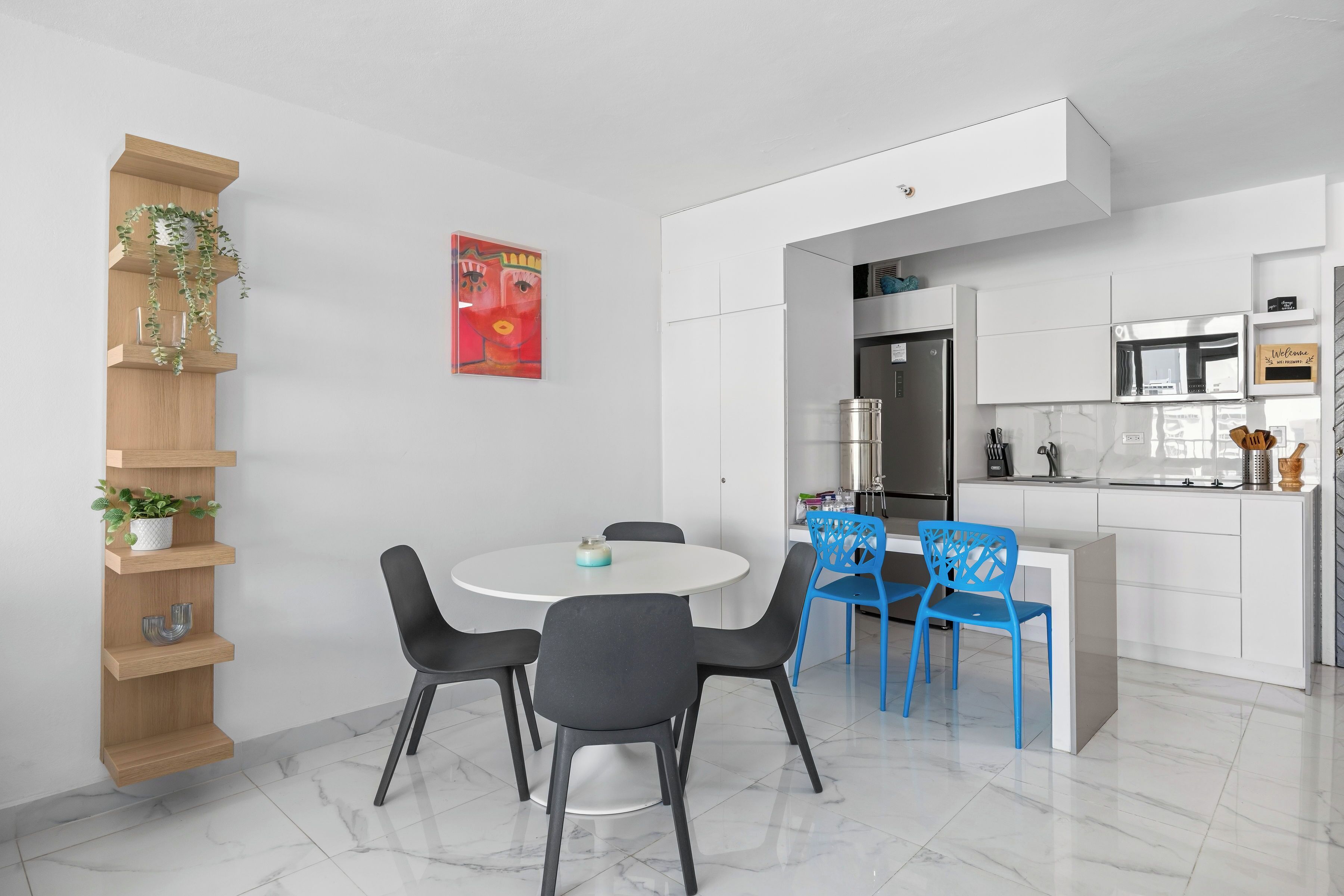 A modern kitchen with white cabinetry, a dining area with a round table and chairs, and a built-in shelf with plants.