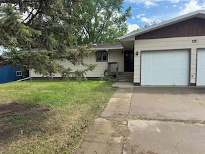 A two-story house with a garage, a front porch, and a tree in the yard.
