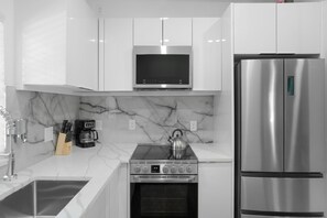 A modern kitchen with white cabinets, a stainless steel refrigerator, a built-in oven, and a microwave.
