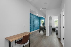 Ein modernes Interieur mit einem Holztisch und Stühlen, einer blauen Akzentwand und einem Flur, der zu einem Schlafzimmer führt.