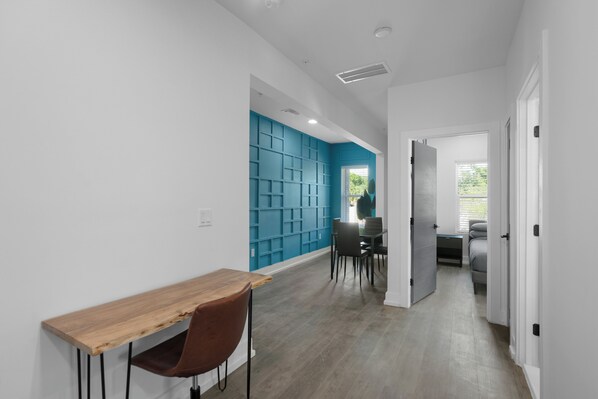 A modern interior with a wooden table and chairs, a blue accent wall, and a hallway leading to a bedroom.