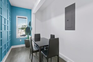 A dining area with a table and chairs, a window with blinds, a potted plant, and a door.