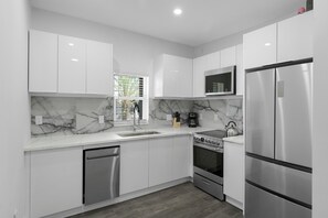 Una cocina moderna con armarios blancos, salpicadero de mármol, electrodomésticos de acero inoxidable y una ventana con persianas.