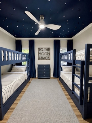 A room with bunk beds, a ceiling fan, a starry ceiling design, a wall with a 'To the Moon & Back' sign, and a grey carpet. - Family Retreat-Reynolds-Sleeps 12-Bunk Room-Lake Oconee Southern Charm Retreat (Greensboro)