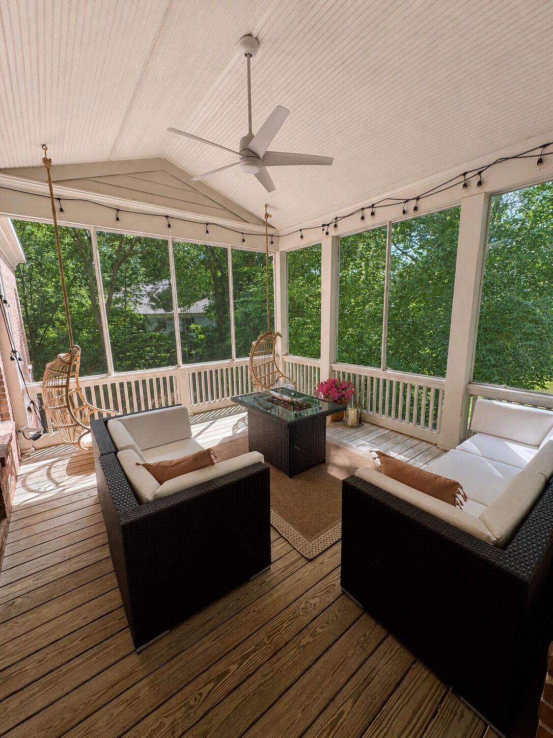 A covered outdoor area with wicker furniture, a glass-top table, and a ceiling fan.