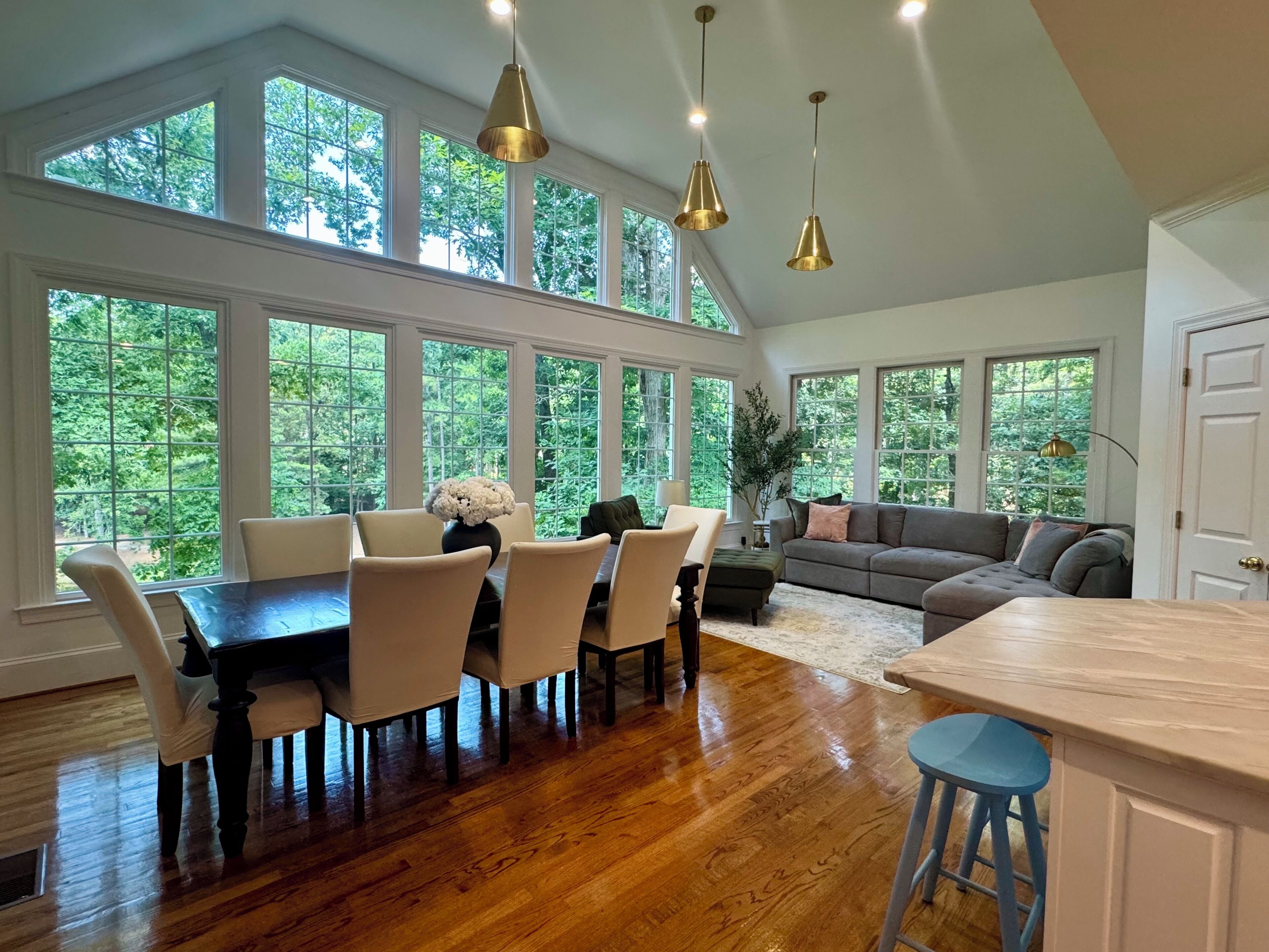 A spacious room with a dining area, a sofa, and large windows.