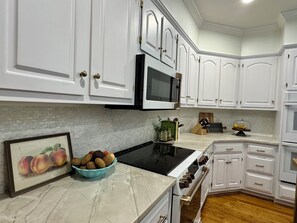 A kitchen with white cabinets, a black microwave, a stove, and a bowl of fruit on the counter. - Family Retreat-Reynolds-Sleeps 12-Bunk Room-Lake Oconee Southern Charm Retreat (Greensboro)