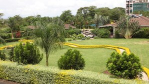 Un jardín ajardinado con diversas plantas y árboles, un pequeño estanque y un edificio con techo rojo.