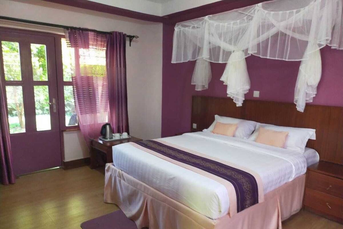 Un dormitorio con cama, cortinas, una mesita de noche y una ventana.