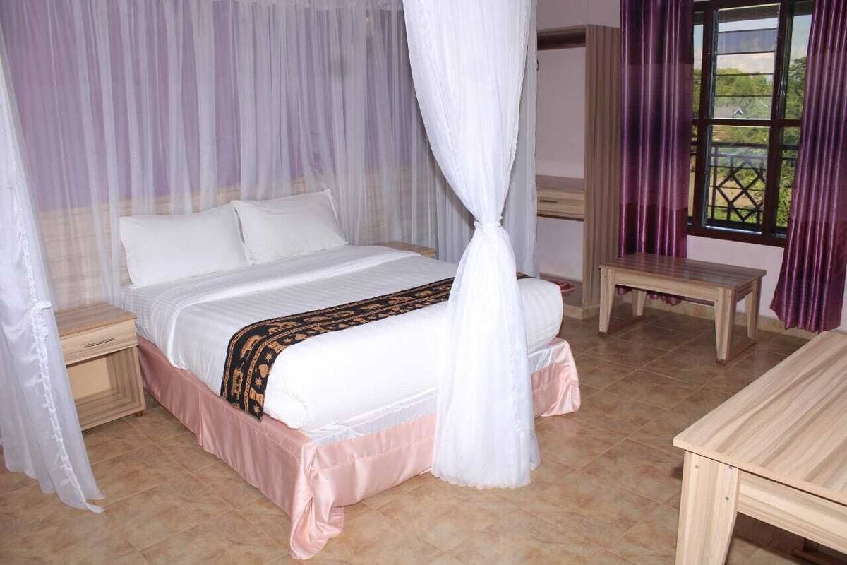 Un dormitorio con cama a dosel, una mesita de noche de madera, una mesa de madera y una ventana con cortinas.