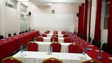 Un salón de conferencias con filas de mesas, sillas rojas y botellas de agua.