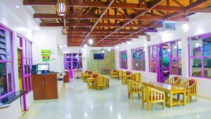 Un comedor con mesas y sillas de madera, una recepción y ventanas grandes con marcos morados.