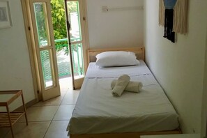Ein Einzelbett mit weißer Bettwäsche, einem hölzernen Kopfteil und zwei zusammengerollten Handtüchern auf dem Bett.
