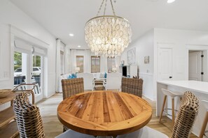 A modern kitchen with a round wooden table, wicker chairs, and a large chandelier. - PRIVATE BEACH/POOL ACCESS-Newly Renovated-Charming Coastal Getaway (Rosemary Beach)