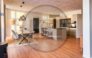A modern kitchen with a central island, bar stools, and a dining area with a glass table and chairs.
