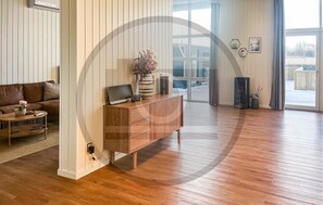 A modern living room with a wooden floor, a brown leather sofa, a wooden cabinet, and a large window.