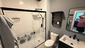 Une salle de bain moderne avec une douche à parois de verre, des toilettes blanches, un lavabo avec un miroir et un porte-serviettes.