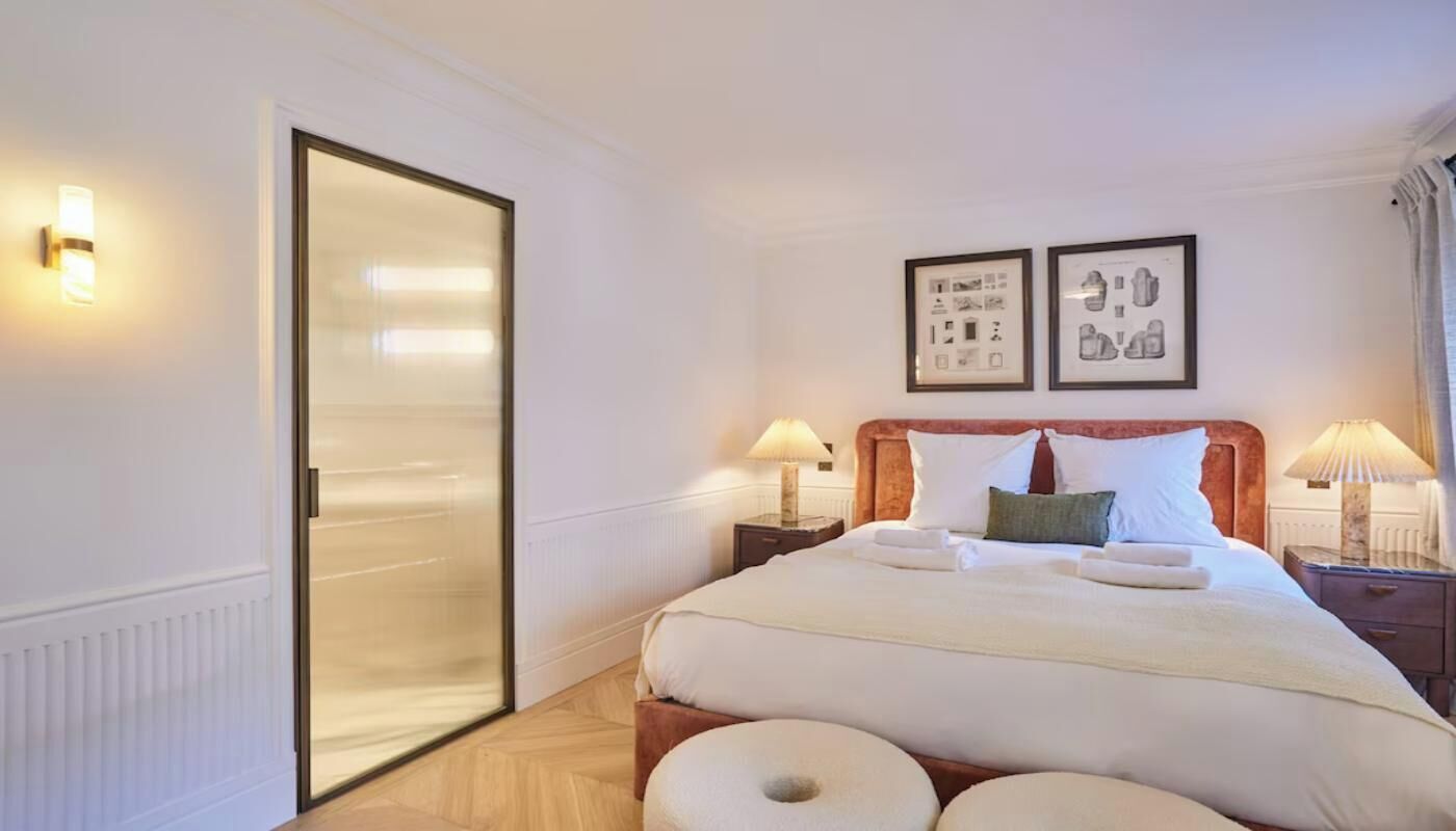 A hotel room with a bed, two bedside tables with lamps, a door, and two framed pictures on the wall.