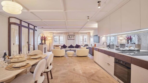 A modern kitchen with a central island, built-in appliances, and a dining area with a sofa and table set for six. - EXPERIENCE PARISIAN ELEGANCE, LOCATED IN BETWEEN INVALIDES & SAINT-GERMAIN (Paris)