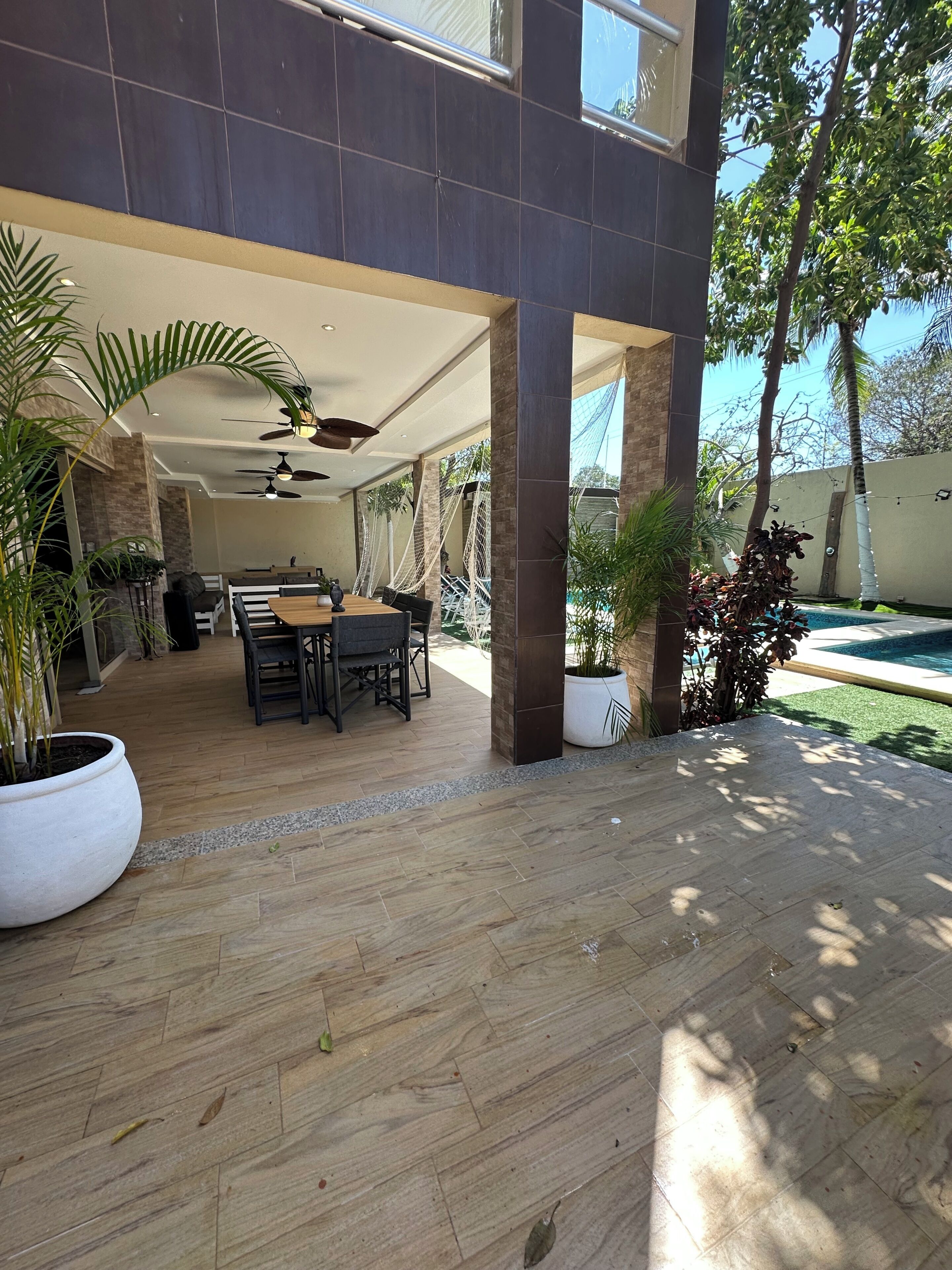 Eine Terrassenanlage im Freien mit Esstisch und Stühlen, umgeben von Kübelpflanzen und einem Pool.