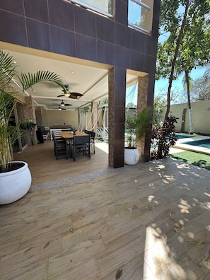 An outdoor patio area with a dining table and chairs, surrounded by potted plants and a pool. - 11-bedroom mansion for 22 guests, plus a rooftop (Playa del Carmen)