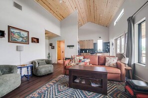 Ein geräumiger Wohnbereich mit hoher Decke, einer Sofagarnitur, einem Couchtisch und einer Küche im Hintergrund.