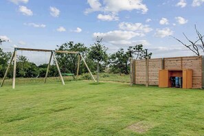 Eine Schaukel aus Holz in einem grünen Garten mit einem Holenzaun und einem Gerätehaus.