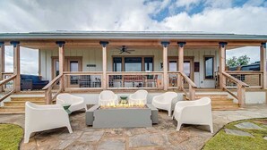 A covered outdoor seating area with a fire pit, white chairs, and a stone patio. - Wylde Skyes | Low-Tox Retreat + Hot Tub (Fredericksburg)