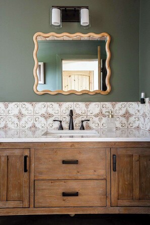 A bathroom with a wooden vanity, two sinks, a mirror, and patterned tiles. - Wylde Skyes | Hot Tub, Fire Pit & Wine Country (Fredericksburg)