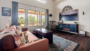 A living room with a sofa, a fireplace, and large windows. - Wylde Skyes | Low-Tox Retreat + Hot Tub (Fredericksburg)