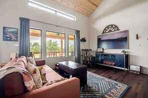 A living room with a sofa, a fireplace, and large windows. - Wylde Skyes | Low-Tox Retreat + Hot Tub (Fredericksburg)