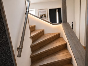 Un escalier en bois avec une rampe métallique, un tableau encadré accroché au mur et une porte en haut.