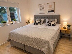A bedroom with a bed, bedside tables, a window, and wall art. - Willa Nordica 3 Bedroom House Garden (Stegna)