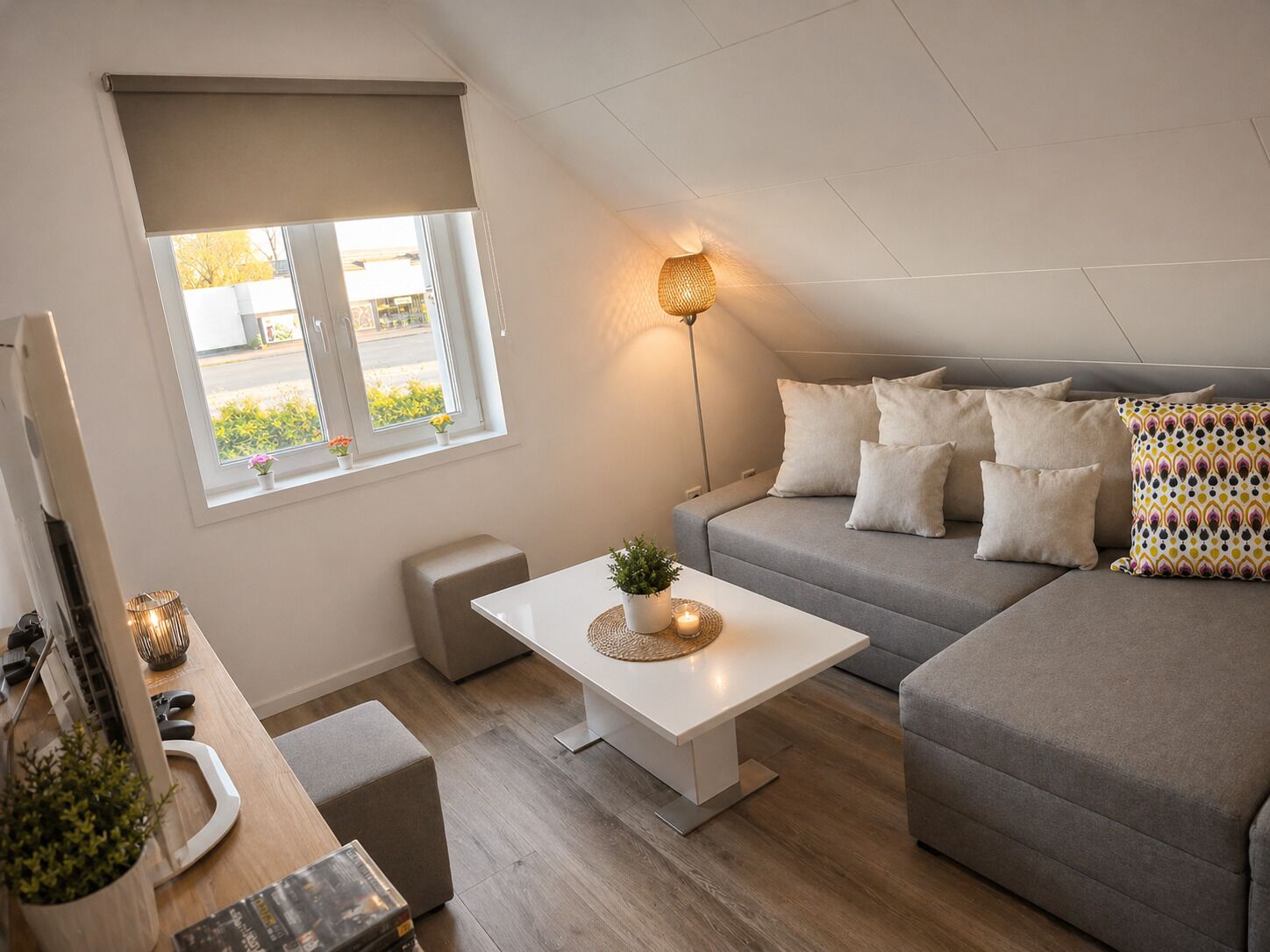 A modern living room with a sofa, a coffee table, a lamp, and a window with a view of the outside.