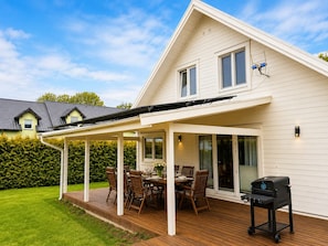 Une maison dotée d’un patio couvert, d’une table à manger avec des chaises et d’un barbecue.