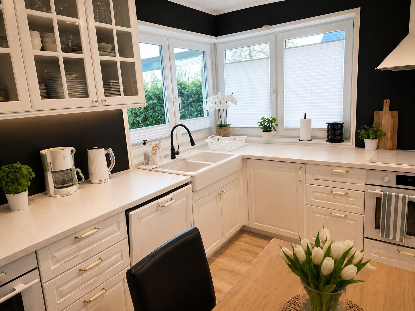 A modern kitchen with white cabinets, a black chair, a coffee maker, and a sink.