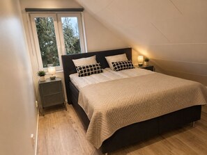 A bedroom with a bed, two bedside tables, a window, and a nightstand. - Willa Nordica 3 Bedroom House Garden (Stegna)