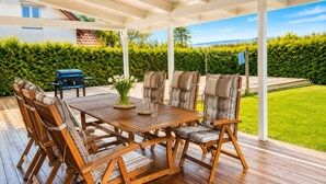 A covered outdoor patio with a wooden table, cushioned chairs, and a grill. - Willa Nordica 3 Bedroom House Garden (Stegna)