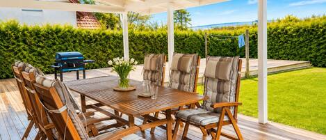 A covered outdoor patio with a wooden table, cushioned chairs, and a grill.