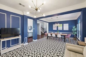 A modern living room with a TV, a patterned rug, a sofa, and a dining area with chairs. - Grand Gem for Large Groups: Pool, Cinema, Playroom (Carrollton)