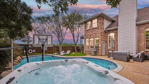 A backyard with a hot tub, a basketball hoop, and a house with a brick exterior. - Grand Gem for Large Groups: Pool, Cinema, Playroom (Carrollton)